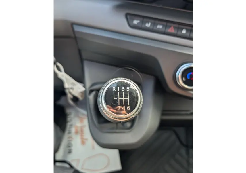 Gros plan sur le levier de vitesses manuel noir du Renault Master blanc, avec tableau de bord et commande de climatisation visibles.