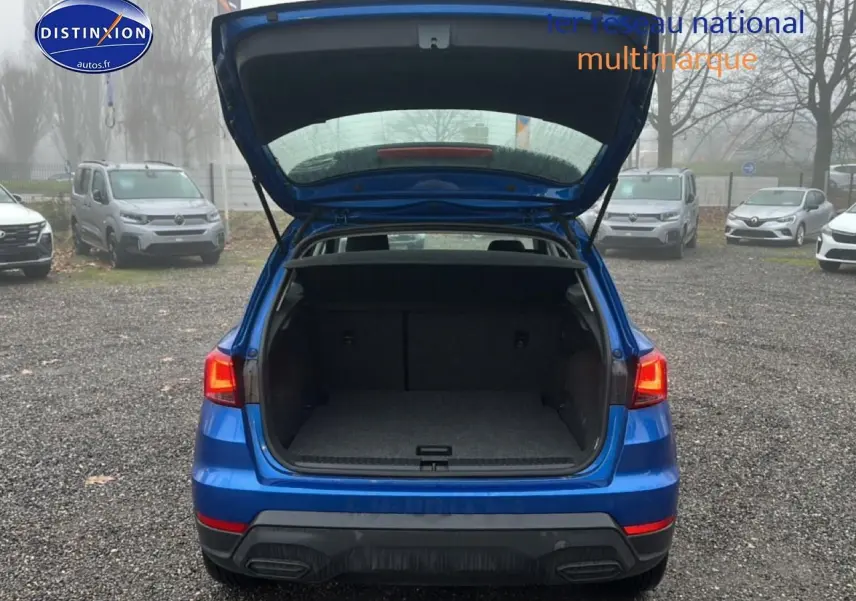 Vue arrière d’un SEAT Arona bleu saphir avec hayon ouvert montrant le coffre vide sur un parking extérieur.