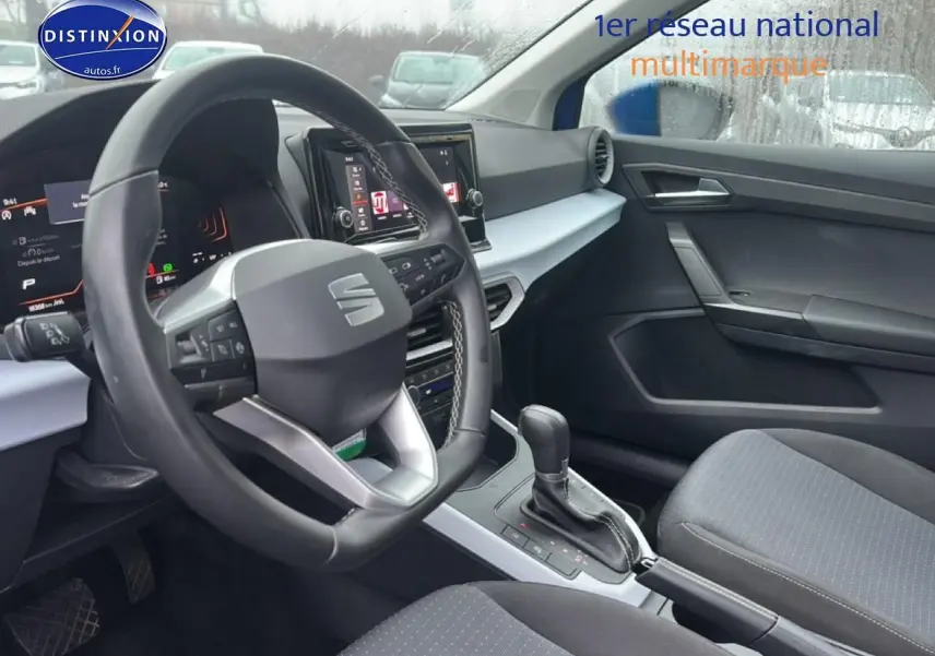 Intérieur avant droit du SEAT Arona 2025, volant cuir méplat, console centrale avec écran tactile et sellerie tissu gris.