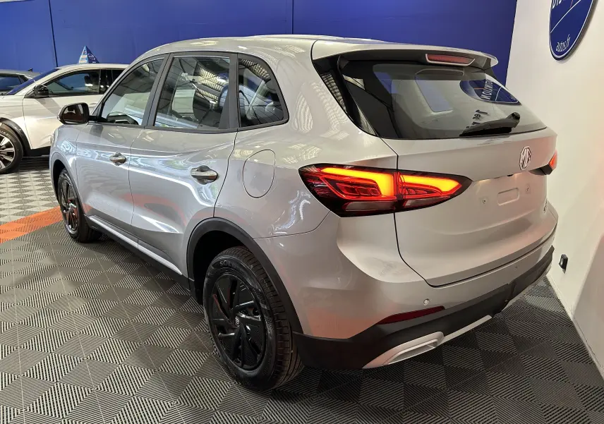 Vue 3/4 arrière droite du MG ZS Cosmic Silver 2025 avec feux allumés et jantes noires en concession.
