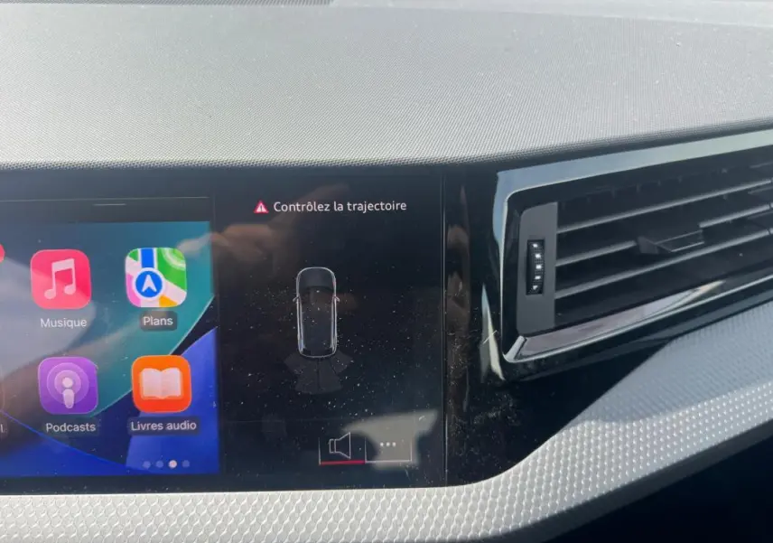 Vue rapprochée du tableau de bord gris de l'Audi A1 Sportback 2025, avec écran tactile affichant l'alerte "Contrôlez la trajectoire".