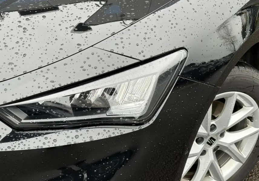 Gros plan sur le phare avant droit et la jante alliage 16 pouces d'une SEAT LEON 2.0 TDI noir Minuit sous la pluie.