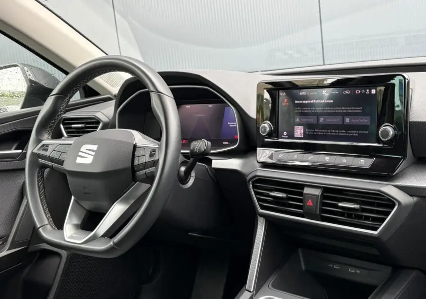 Vue intérieure côté conducteur du tableau de bord du SEAT Leon 2024 avec écran tactile et volant multifonction noir.