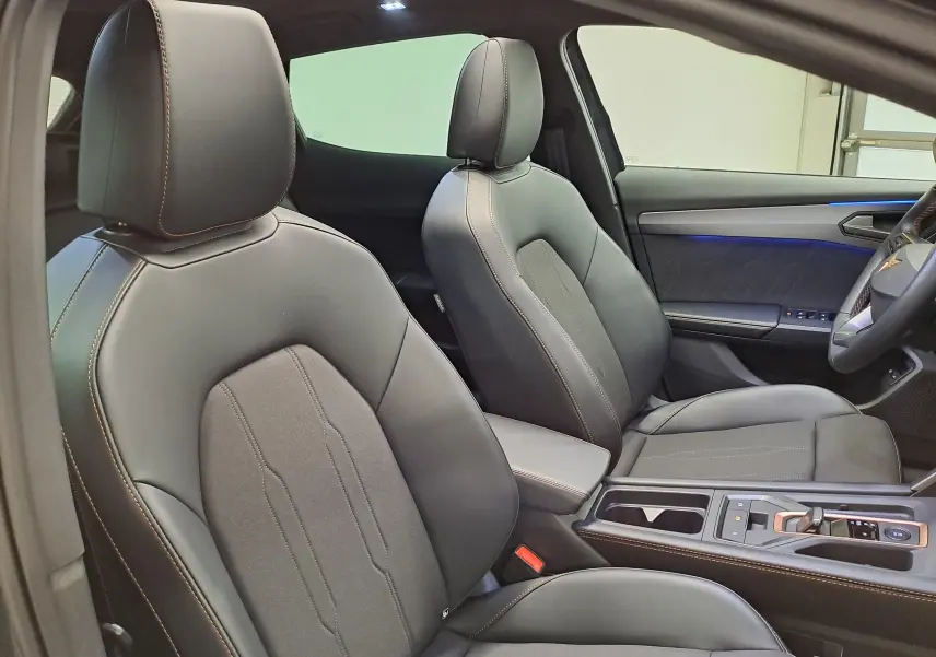 Vue intérieure côté droit montrant les sièges avant en cuir noir avec surpiqûres cuivrées et éclairage d'ambiance bleu sur la porte.