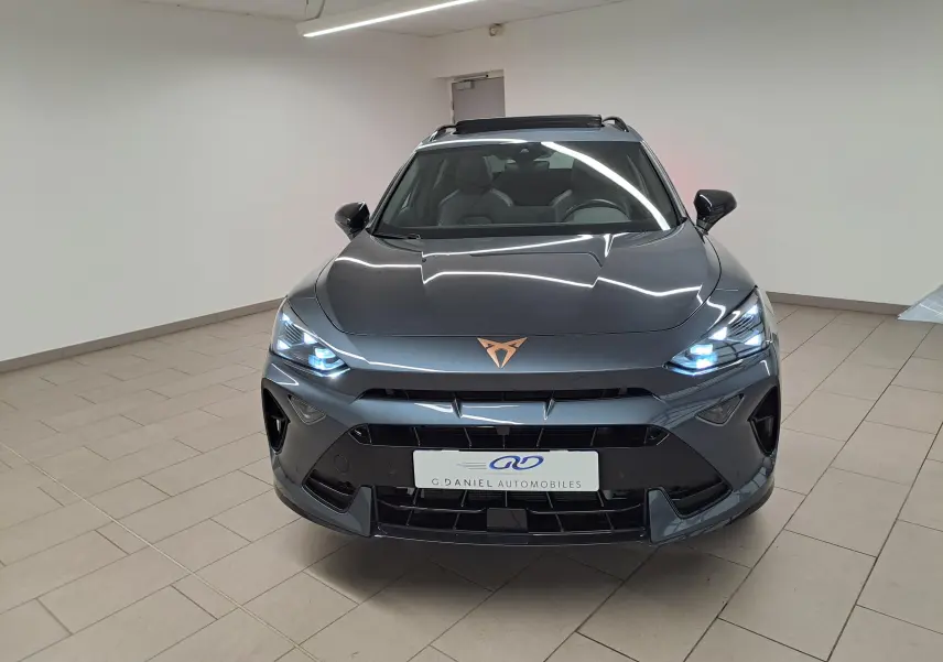 Vue frontale d'un CUPRA Formentor gris magnétique avec logo cuivré et phares LED allumés dans un showroom.