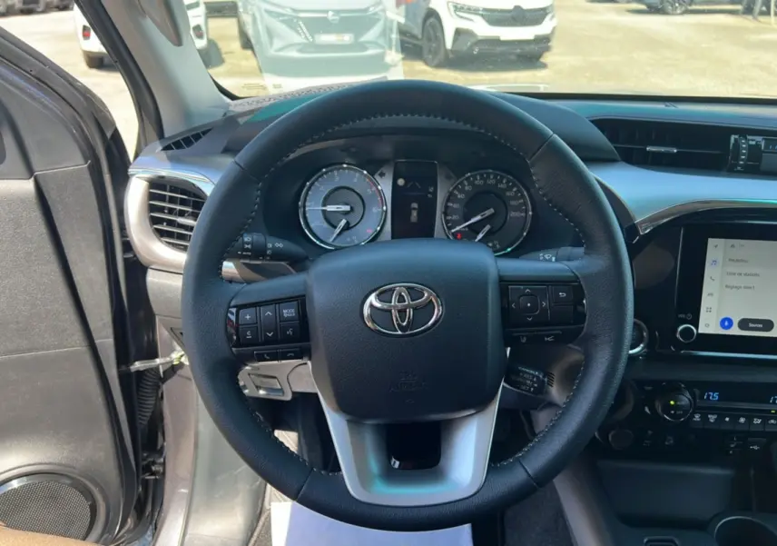 Vue intérieure centrée sur le volant cuir multifonctions du Toyota Hilux 2026, avec tableau de bord et écran tactile visible.