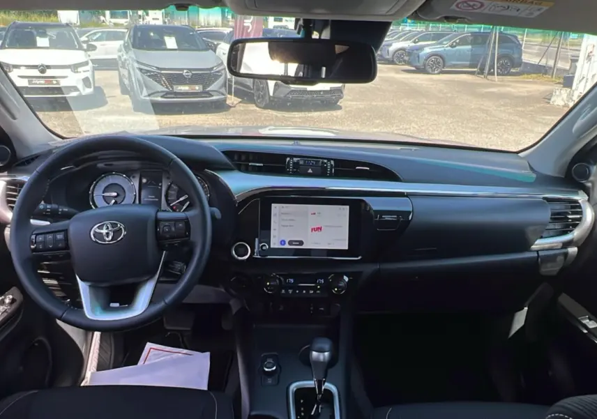Vue intérieure avant du Toyota Hilux 2026, tableau de bord noir avec écran tactile central et volant multifonctions.