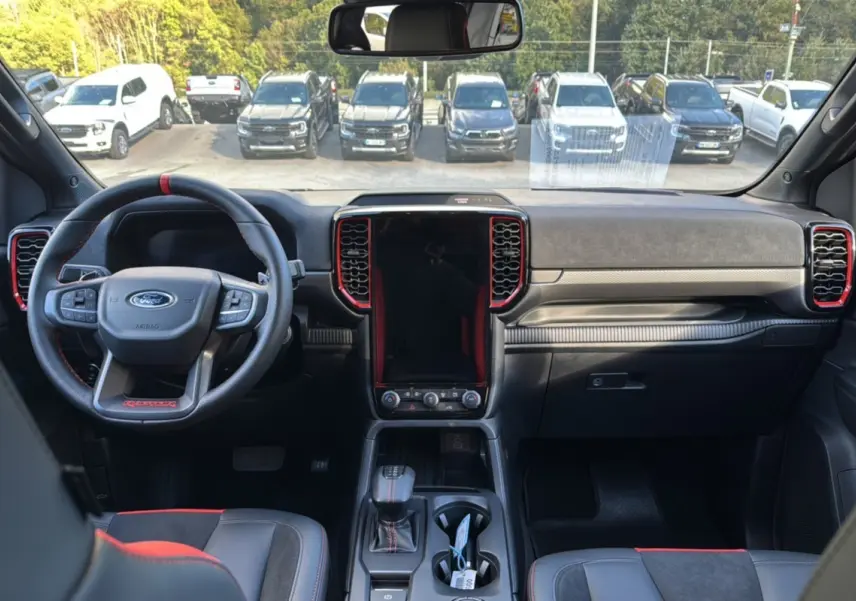 Vue intérieure avant du Ford Ranger Raptor 2024 noir absolu, avec volant sport et console centrale tactile verticale.