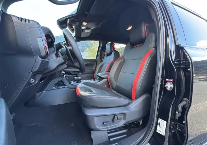 Vue intérieure côté conducteur du Ford Ranger Raptor 2024 noir absolu, sièges sport noirs avec surpiqûres rouges.