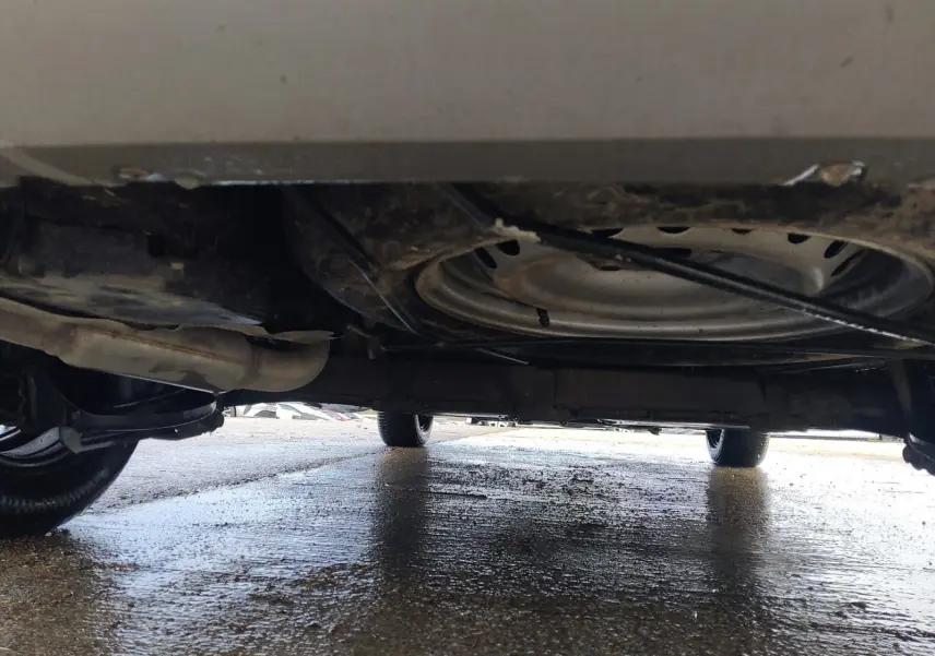 Vue sous le Renault Kangoo blanc 2022, montrant la roue de secours et le châssis sur sol humide.