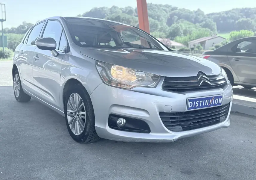 Citroën C4 gris vue 3/4 avant droit avec phare allumé, calandre noire et jantes alliage.