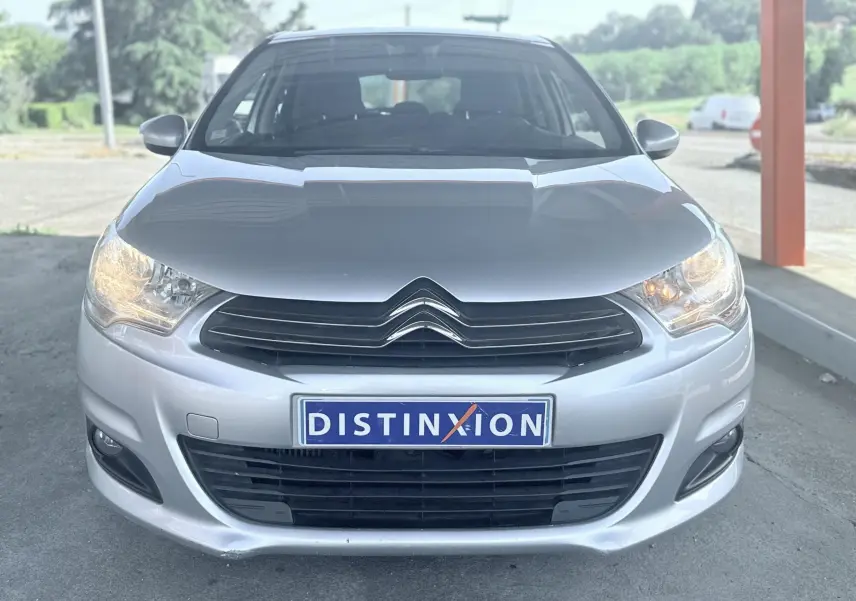 Vue frontale d'une Citroën C4 gris métallisé avec phares allumés et plaque d'immatriculation Distinxion.