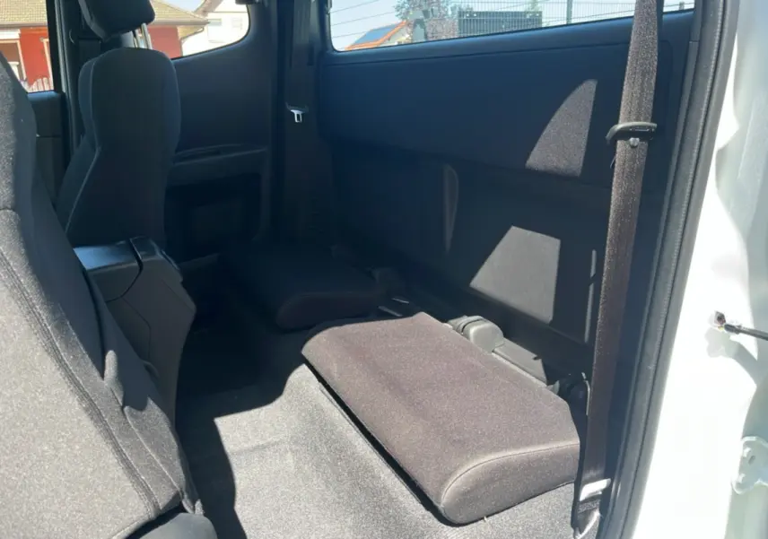 Vue intérieure arrière droite du pick-up Isuzu D-MAX 2026 blanc, montrant les strapontins rabattus en tissu noir.