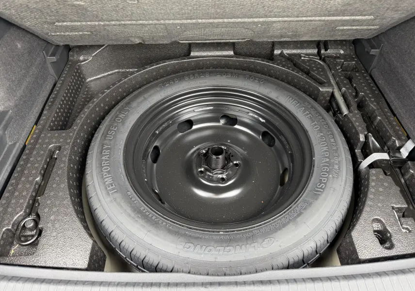Gros plan sur la roue de secours compacte noire dans le coffre du Volkswagen Tiguan gris 2025.
