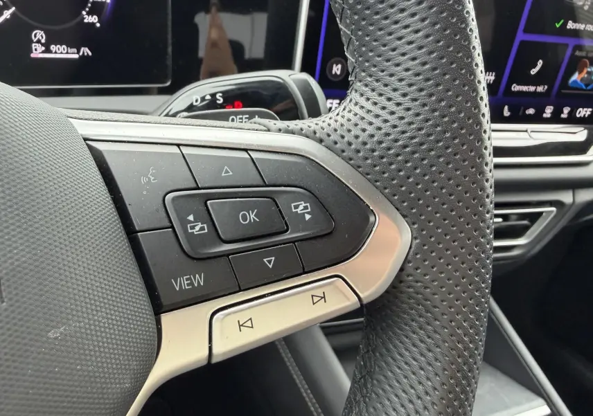 Gros plan sur la partie gauche du volant cuir perforé du Volkswagen Tiguan 2025 avec commandes multifonctions et tableau de bord numérique.