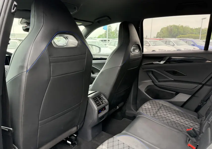 Vue intérieure arrière du Volkswagen Tiguan 2025 avec sièges sport noirs et surpiqûres bleues, ambiance raffinée.