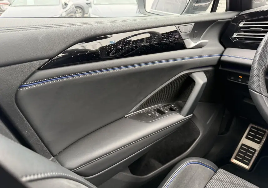 Vue intérieure côté gauche du Volkswagen Tiguan 2025, avec garniture cuir noire et surpiqûres bleues sur la porte.