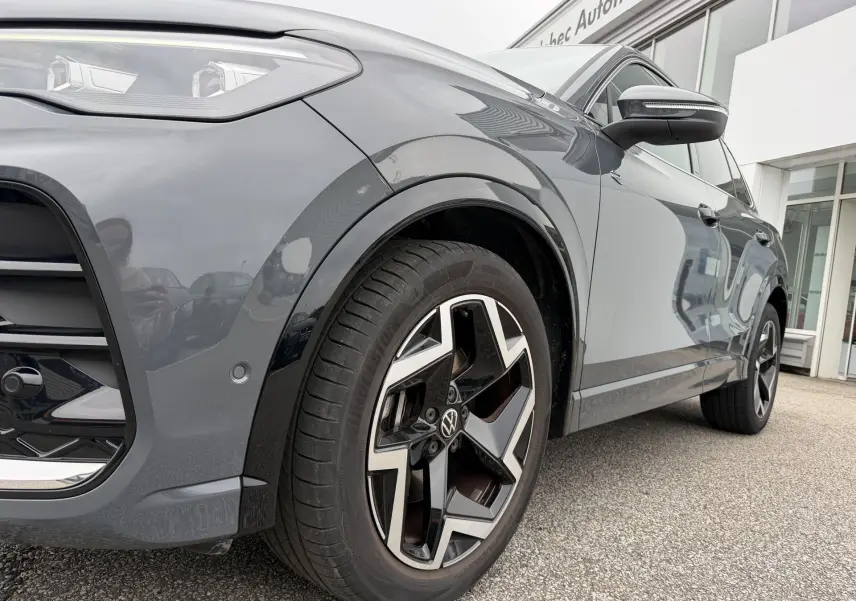 Vue de profil côté avant droit d’un Volkswagen Tiguan gris avec jantes alliage 19 pouces au design distinctif.