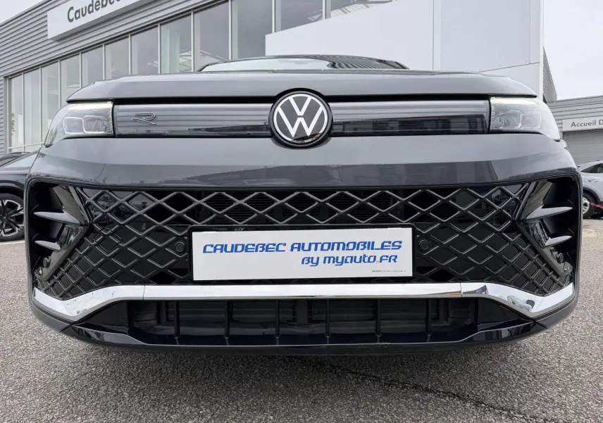 Vue frontale rapprochée du Volkswagen Tiguan gris 2025 avec calandre noire à motif losange et logo VW central lumineux.