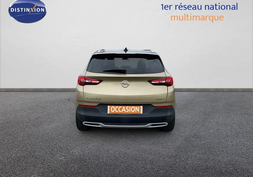 Vue arrière d'un Opel Grandland X diesel couleur golden sunstone metal avec plaque occasion sur un sol gris.