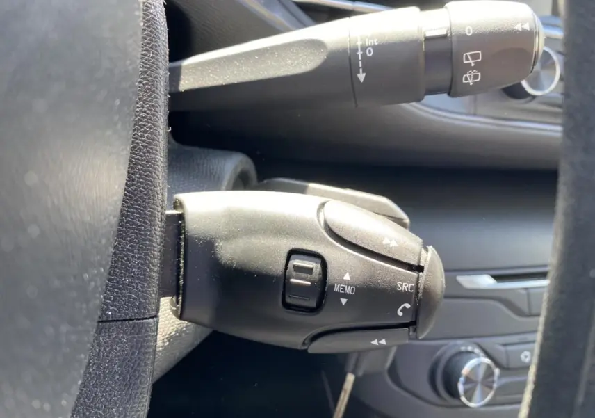 Gros plan sur la commande multifonction noire côté gauche du volant d'une Peugeot 308 SW gris clair, avec tableau de bord en arrière-plan.