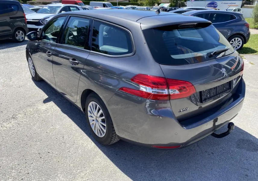 Peugeot 308 SW gris clair vue 3/4 arrière droit avec attelage et feux arrière distinctifs au soleil.