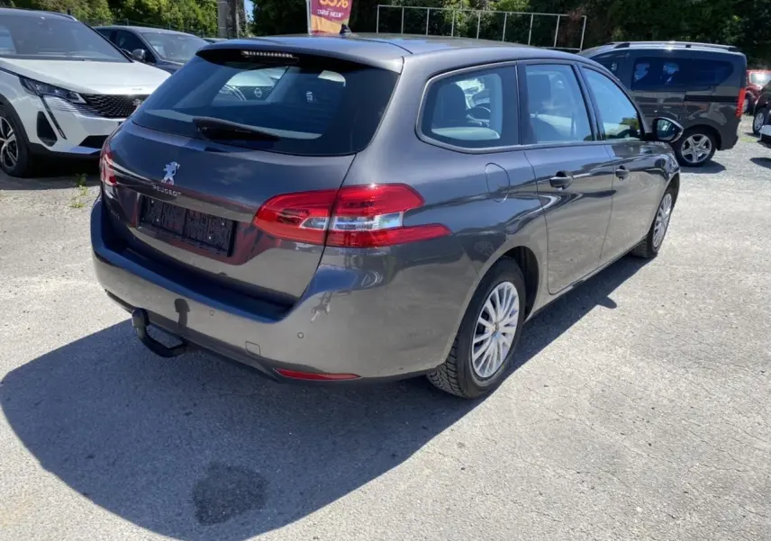 Peugeot 308 SW gris clair vue 3/4 arrière droit avec attelage de remorque sur un parking ensoleillé.
