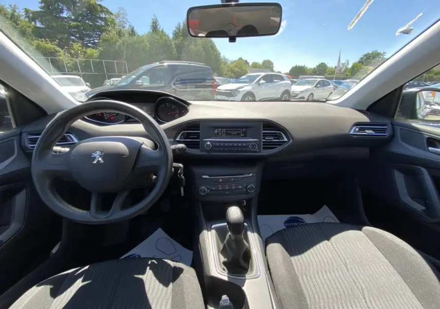 Vue intérieure avant de la Peugeot 308 SW gris clair de 2017, volant, tableau de bord et levier de vitesse manuelle visibles.