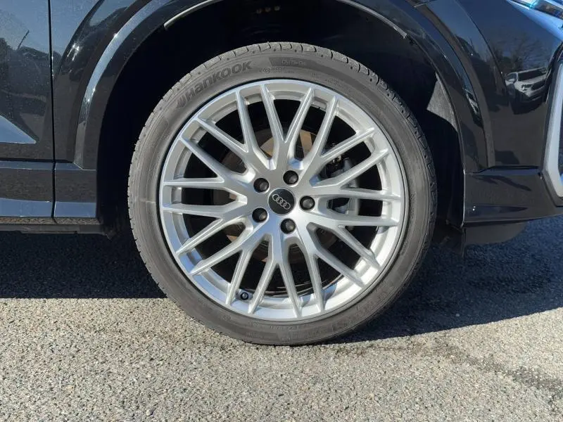 Gros plan sur la roue avant droite de l'Audi Q2 noire Mythic métallisée avec jante alu multi-branches argentée.