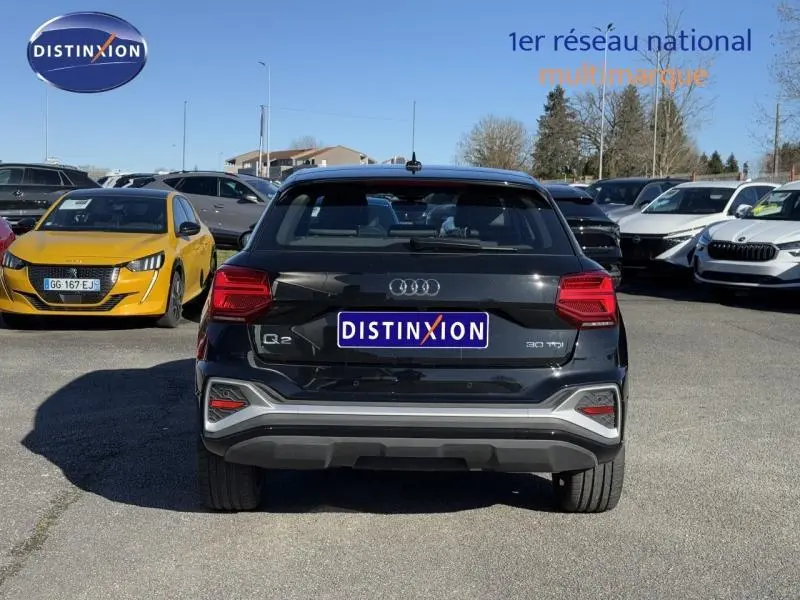 Vue arrière d'un Audi Q2 noir Mythic métallisé 2024, avec feux LED et logo distinctif sur un parking extérieur.