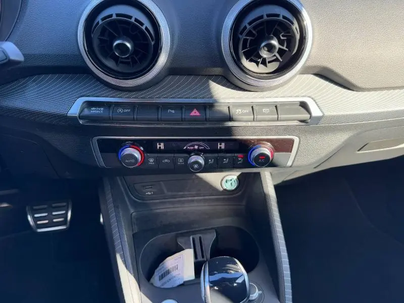 Vue rapprochée du tableau de bord et console centrale de l'Audi Q2 noir Mythic, avec commandes climatisation et ventilation circulaire.