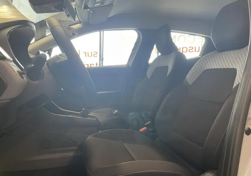 Intérieur Renault Clio 1.5 Blue dCi 2025 vu côté gauche, sièges tissu gris à motifs 3D et volant multifonction.