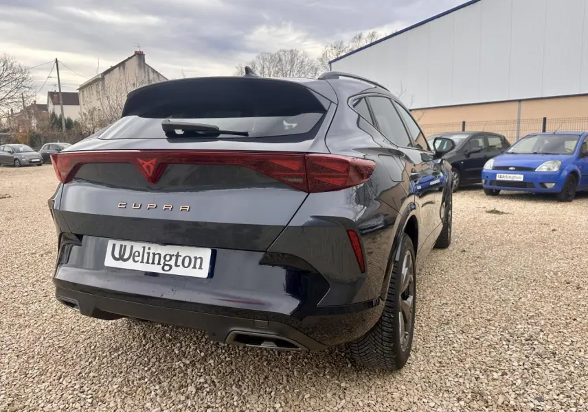 Vue 3/4 arrière droite d'une CUPRA Formentor gris foncé avec feux arrière triangulaires et logo rouge distinctif.