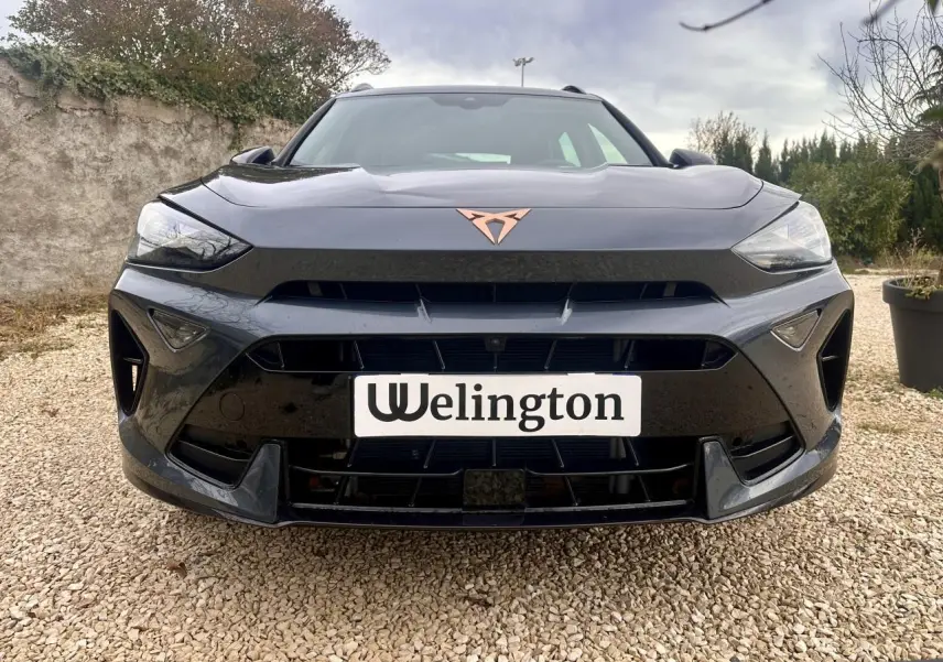 Vue avant d'une CUPRA Formentor gris foncé avec logo cuivre et calandre large sur un sol gravillonné.