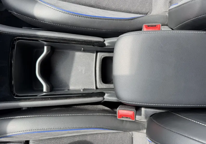 Vue plongeante sur la console centrale du Volkswagen Tiguan gris, avec accoudoir cuir noir et surpiqûres blanches.
