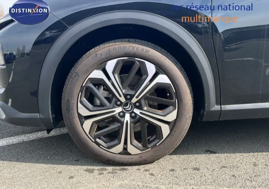 Gros plan sur la roue avant droite de la Citroën C5 X noire métal, mettant en valeur la jante alliage bicolore moderne.