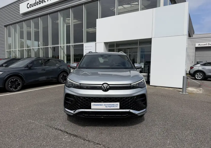 Vue avant d'un Volkswagen Tiguan gris métallisé 2025 avec calandre noire et phares LED, devant un concessionnaire.