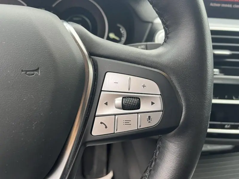 Gros plan sur les commandes multifonctions à droite du volant cuir noir d'une BMW X3 xDrive30eA 2020 Glaciersilber.