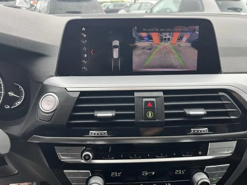 Vue intérieure du tableau de bord du BMW X3 xDrive30e 2020 avec écran tactile affichant la caméra de recul et commandes climatisation tri-zone