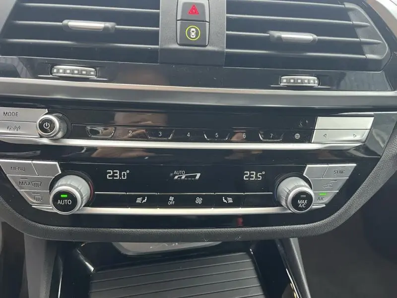 Détail de la console centrale avec commandes de climatisation automatique bi-zone et boutons multifonctions d'une BMW X3 xDrive30eA Glacier Silver de 2020.