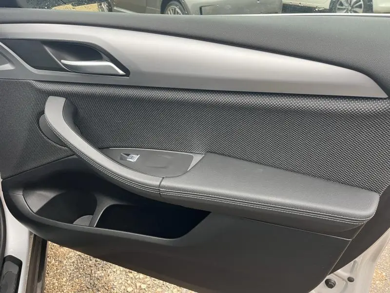 Intérieur de la porte côté gauche d'une BMW X3 Glacier Silver 2020, avec poignée et habillage noir texturé.