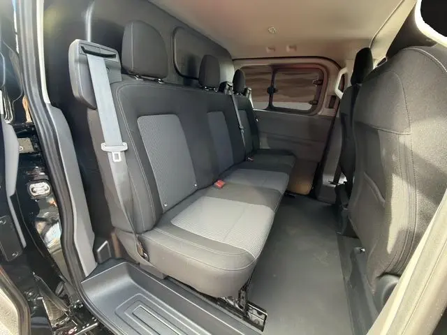 Vue intérieure côté droit du Volkswagen Transporter ProCab noir, montrant la banquette arrière en tissu rayé et les fenêtres latérales assombries.