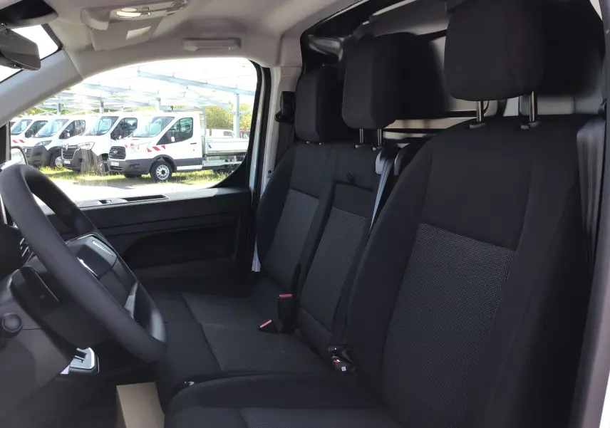 Vue intérieure côté conducteur du Peugeot Expert Fourgon blanc 2025, montrant les sièges noirs et la cabine utilitaire.