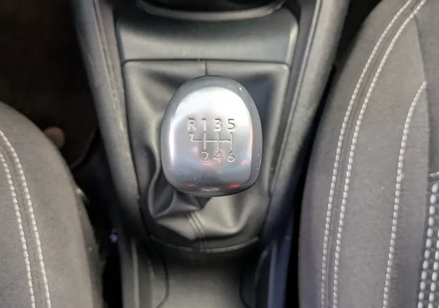 Vue plongeante sur le levier de vitesses manuel argenté entouré de sièges noirs avec surpiqûres blanches dans une Peugeot 208 noire.