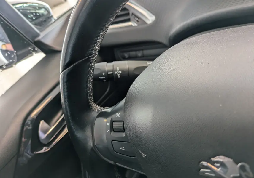 Gros plan sur le volant noir de la Peugeot 208 Allure 2019, montrant les commandes intégrées côté gauche du tableau de bord.
