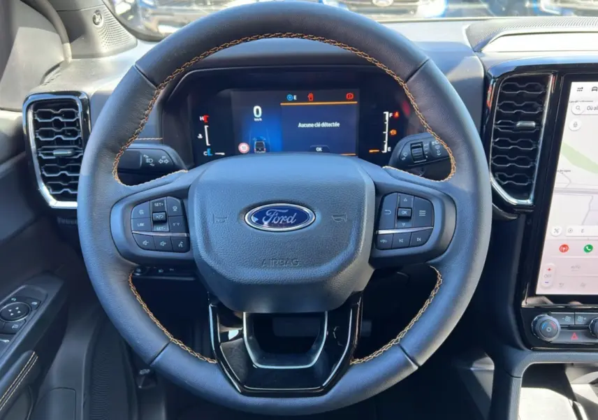 Vue rapprochée du volant en cuir noir avec surpiqûres marron du Ford Ranger 2025 gris carbone, tableau de bord digital et écran tactile.