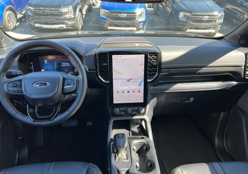 Vue intérieure du Ford Ranger Wildtrak Plus 2025 montrant le tableau de bord noir avec écran tactile vertical et volant multifonction.
