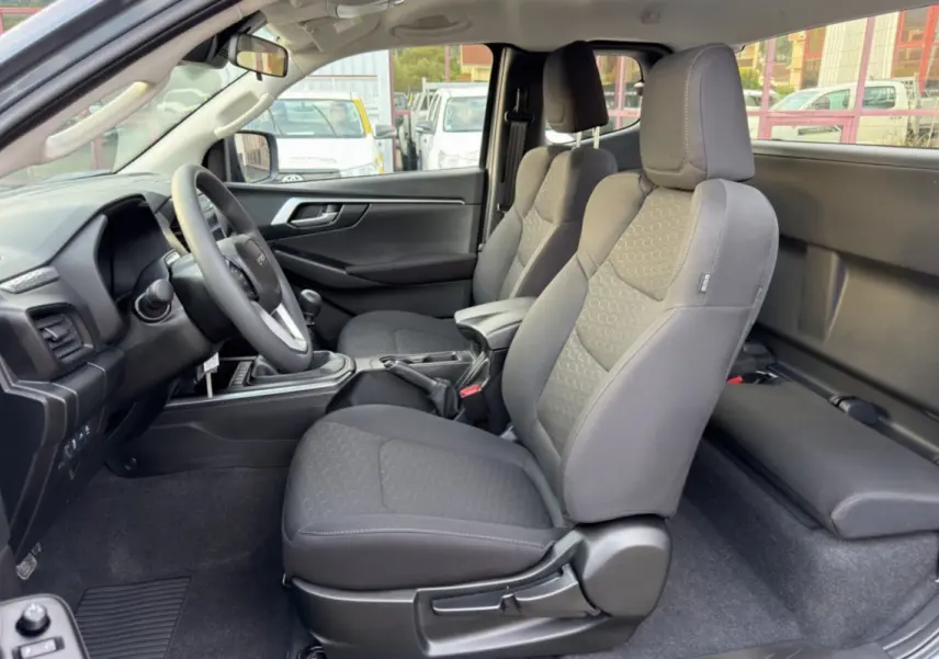 Intérieur du pick-up Isuzu D-MAX 2026, vue côté gauche sur les sièges tissu gris et le volant multifonctions.