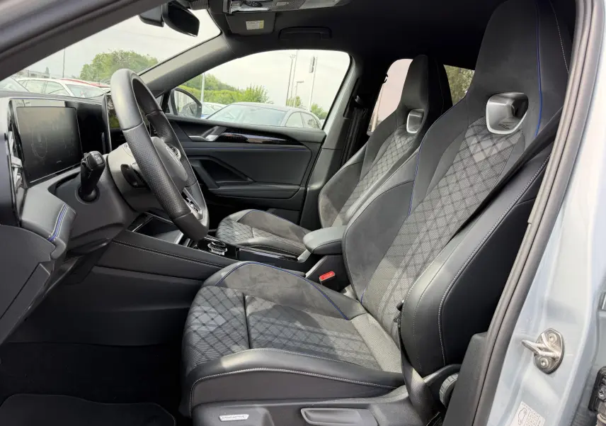 Vue intérieure côté conducteur du Volkswagen Tiguan 2025, sièges sport gris avec surpiqûres bleues et volant multifonction cuir.