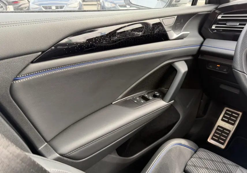 Vue intérieure côté gauche du Volkswagen Tiguan 2025, porte en cuir noir avec surpiqûres bleues et commandes électriques.
